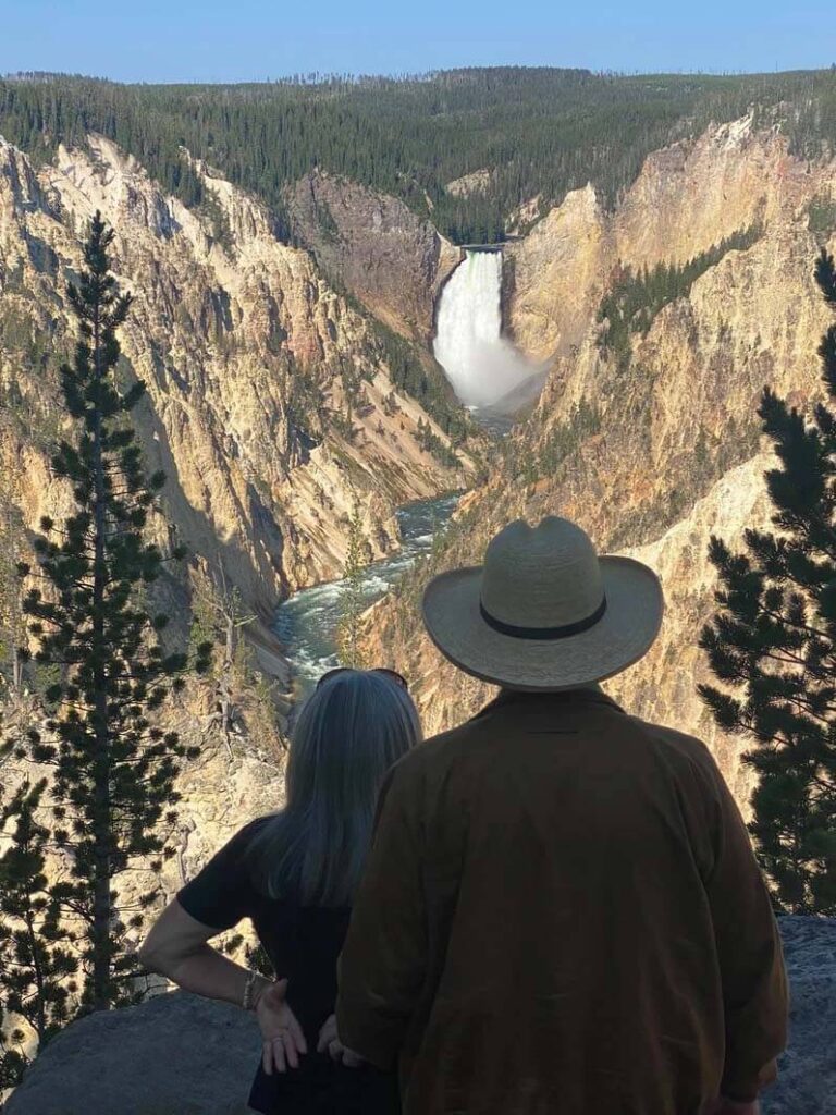 A couple observes Yellowstone Falls at Artist Point Overlook. Taken on a private tour with Teton Excursions in Yellowstone National Park.