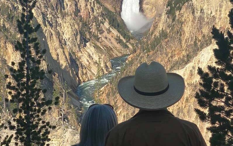 A couple observes Yellowstone Falls at Artist Point Overlook. Taken on a private tour with Teton Excursions in Yellowstone National Park.